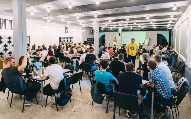 Large room with people at tables, a presenter at the front, and motivational text on the walls